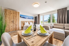 A modern hotel room with a wooden dining table set for two, a sofa, and a bed with a mountain view. - Smart Resorts - Haus Diamant - Studio-apartment 708 mit Balkon, Max. 4 Personen - Smart Resorts Haus (Winterberg)