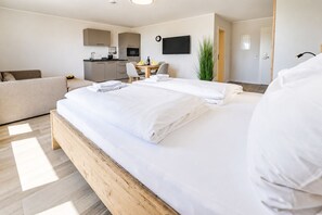 Habitación de hotel con una cama de madera, una kitchenette pequeña, una mesa de comedor con sillas y un televisor montado en la pared.