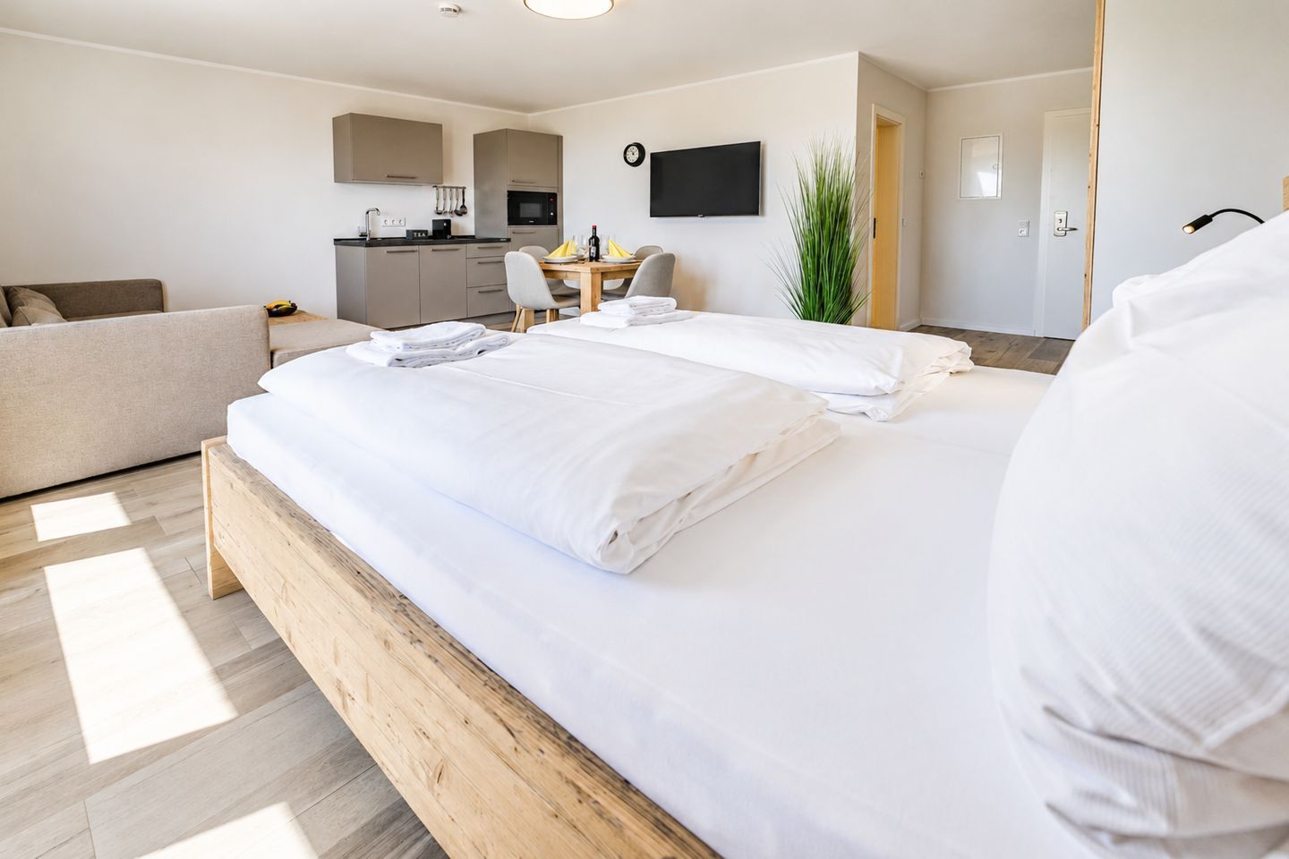 Ein Hotelzimmer mit einem Holzbett, einer kleinen Küchenzeile, einem Esstisch mit Stühlen und einem an der Wand befestigten Fernseher.