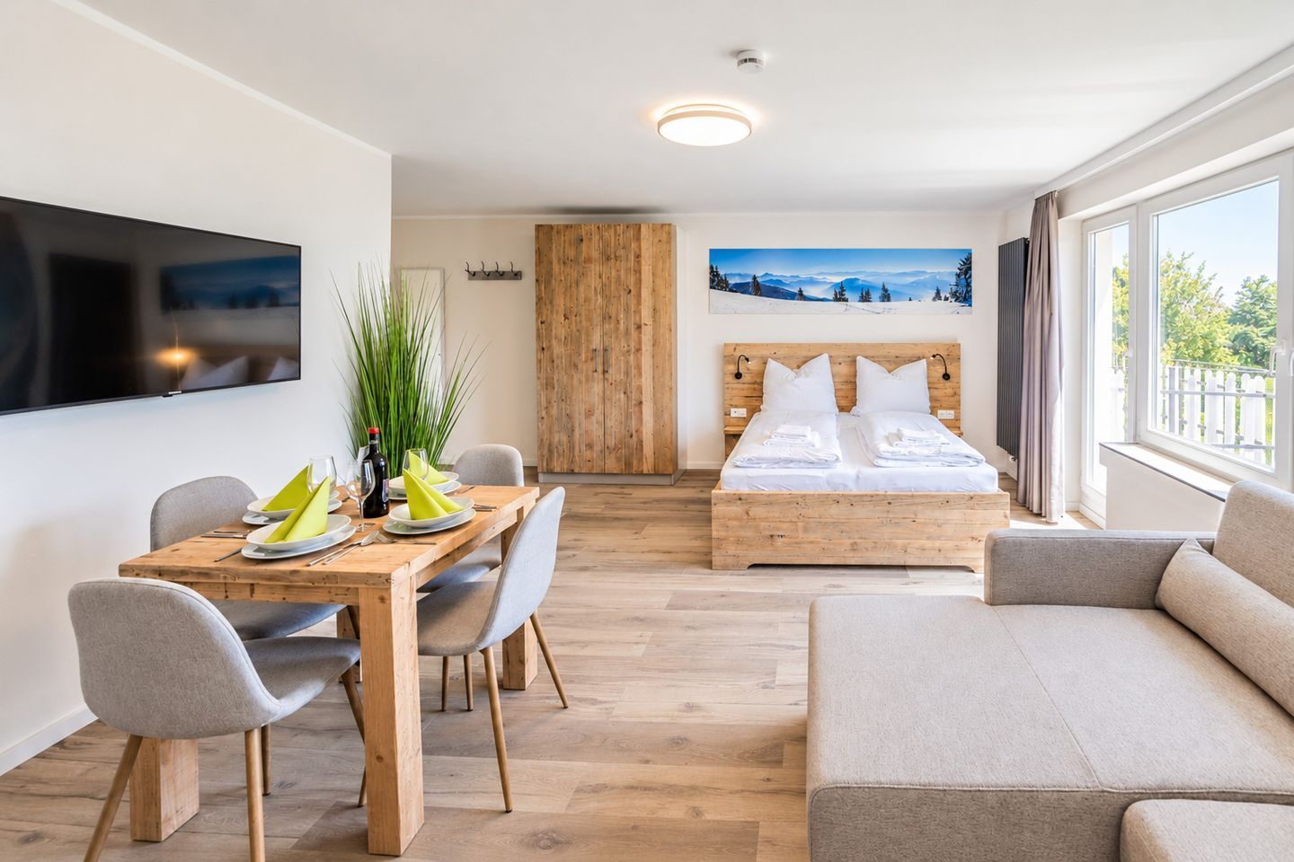 Ein modernes Hotelzimmer mit einem hölzernen Bett, einem Essbereich mit Tisch und Stühlen, einem Flachbildfernseher und einem großen Fenster mit Blick.