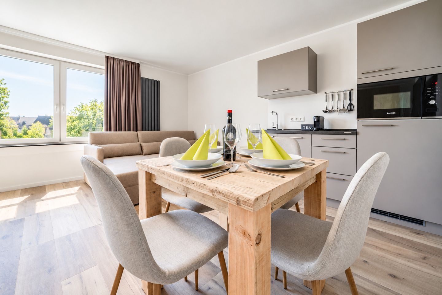 A modern kitchen with a built-in oven and a dining area with a wooden table and grey chairs.