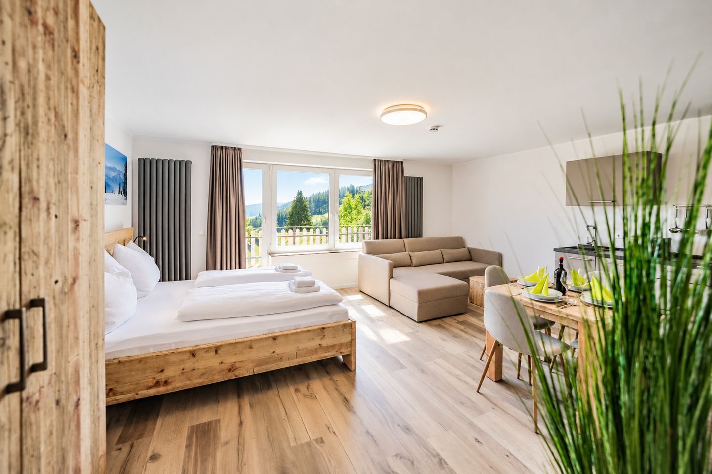 A modern hotel room with a wooden bed, a sofa, a dining table, and a view of the outdoors.