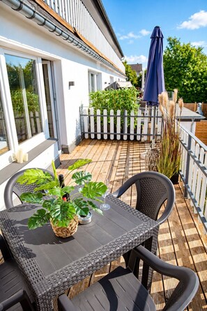 Una terraza con mesa y sillas, una planta en maceta y un paraguas azul.