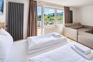 A hotel room with a bed, a sofa, and a balcony with a view of trees and hills.