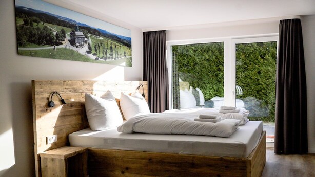 A bedroom with a wooden bed, white bedding, and a large window with curtains.