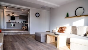 A modern living room with a grey sofa, a wooden coffee table, and a kitchen in the background.