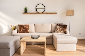Ein modernes Wohnzimmer mit einer Eckcouch, einem Holztisch, einem runden Spiegel und einer Stehlampe.