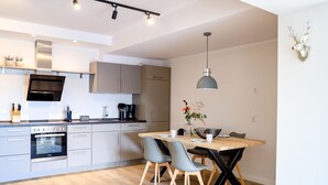 A modern kitchen with a built-in oven, a dining table with chairs, and a pendant light.