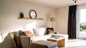 A modern living room with a sofa, ottoman, and a small coffee table. There is a mirror on the wall and a lamp beside the sofa.
