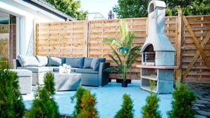 An outdoor patio with a grey sofa, a small table, and a stone oven.
