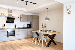 A modern kitchen with a dining area, featuring a built-in oven, a coffee machine, and a dining table with chairs.