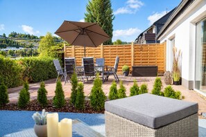 An outdoor patio area with a table and chairs, a wooden fence, and a view of a hilly landscape.