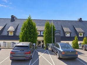 Un hotel con diseño moderno, que cuenta con un estacionamiento con dos autos, un cartel y un césped bien cuidado.