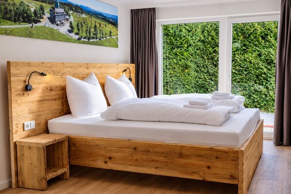 Una cama de madera con ropa de cama y almohadas blancas, una mesita de noche y una lámpara de pared.