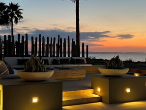 An outdoor seating area with sofas and planters, overlooking a body of water at sunset. - Beach front paradise, Island living in La Paz (La Paz BCS)