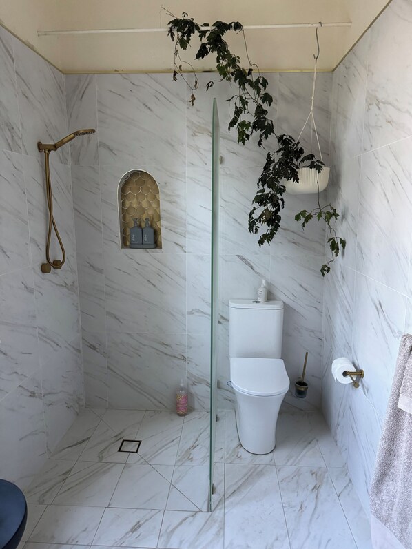 Un baño con paredes de mármol, ducha con puerta de vidrio, inodoro y lavamanos.