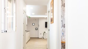 A hallway with a wooden floor, white walls, and a door at the end. There are framed pictures on the wall and a small plant on the floor. - Cottage with pool, barbecue and garden (Nigüelas)