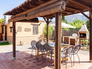 A covered outdoor patio with a table and chairs, a barbecue grill, and a stone building in the background. - Cottage with pool, barbecue and garden (Nigüelas)