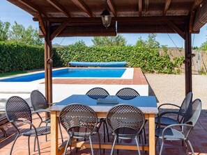 En udendørs terrasse med pool, overdækket loungeområde og udsigt over poolen.
