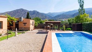 A swimming pool with a patio area, a covered seating area, and a view of mountains in the background. - Cottage with pool, barbecue and garden (Nigüelas)