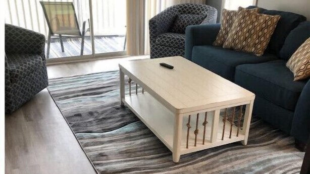 Una sala de estar con una mesa de centro de madera, un tapete estampado y un sofá azul oscuro con cojines decorados.