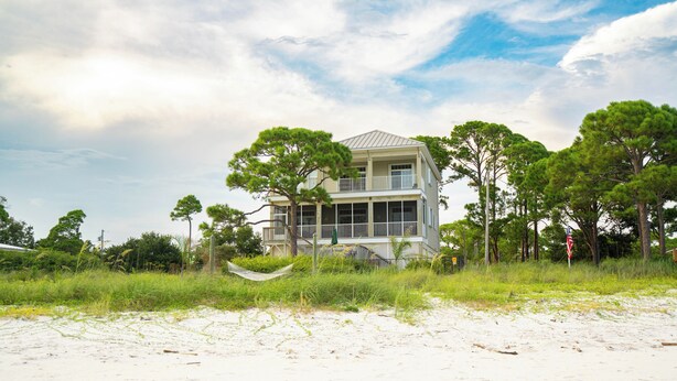 Une maison située en bord de mer, dotée d’un balcon, entourée d’arbres et agrémentée d’un hamac.