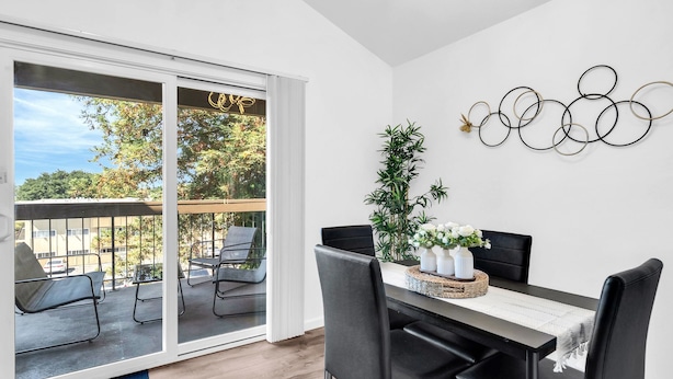 Un'elegante sala da pranzo con una grande porta scorrevole in vetro che si apre su un balcone esterno, un tavolo da pranzo nero con sedie e un elemento decorativo a parete.