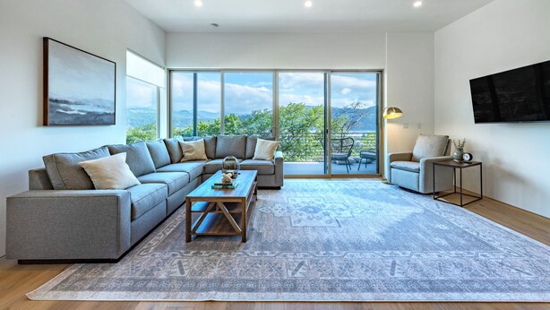 Un salón amplio con un sofá grande, una mesa de centro y vistas a través de ventanas grandes.