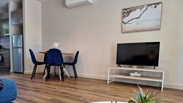 Un salon moderne avec un coin repas, un téléviseur à écran plat posé sur un meuble blanc et une plante en pot sur une table blanche.