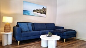 Un salon moderne avec un canapé bleu, une table basse ronde et une lampe sur une table d’appoint.