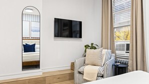 Een moderne slaapkamer met een bed, een televisie, een gestreept fauteuil en een raam met gordijnen.