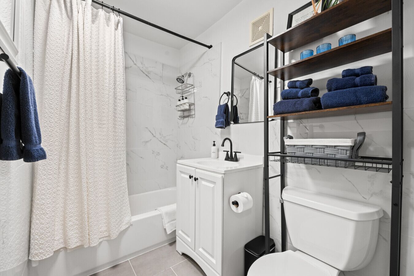 A modern bathroom with a shower, toilet, and sink. There are towels and toiletries on shelves.