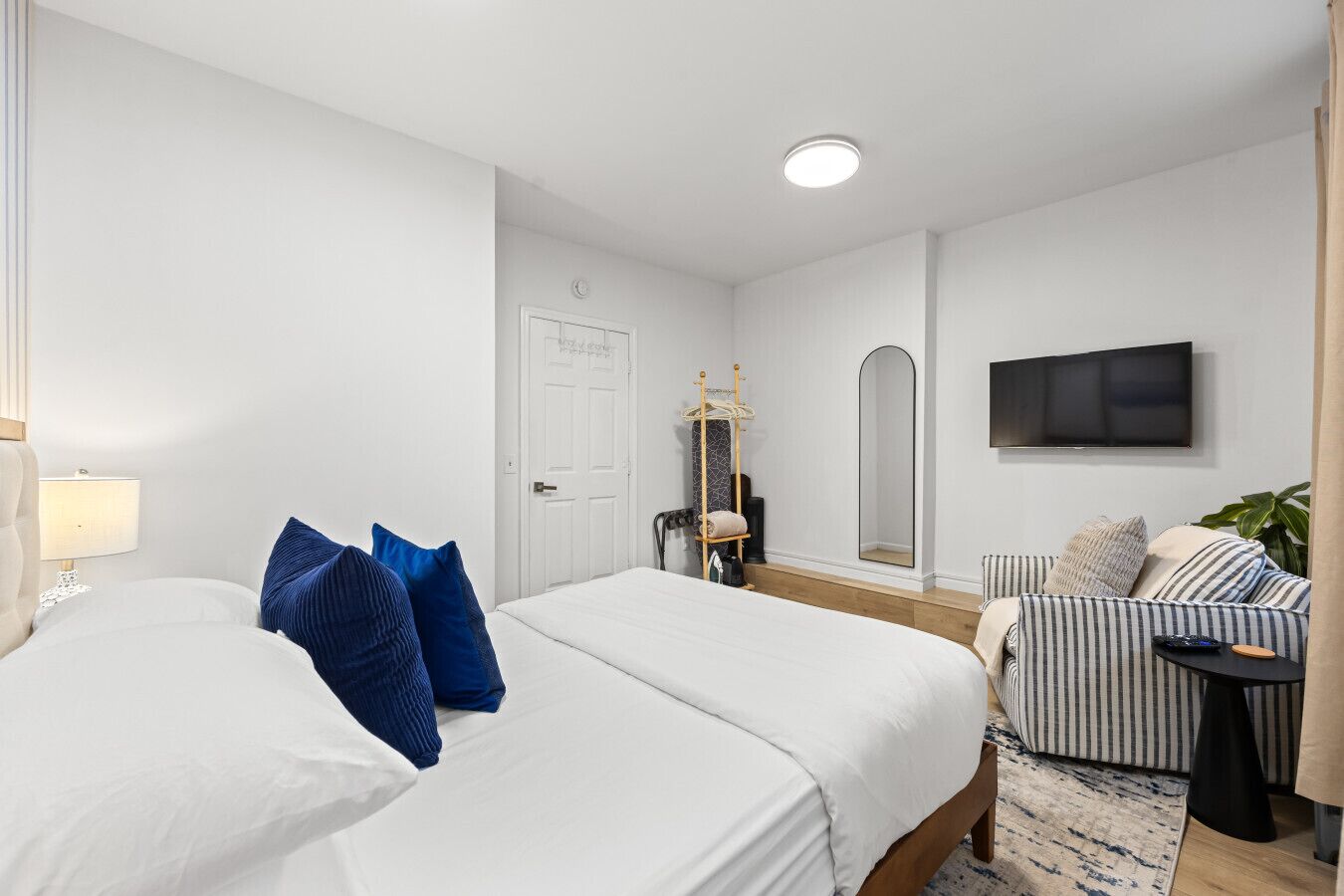 Une chambre d’hôtel avec deux lits, un téléviseur, un porte-manteau et un fauteuil à rayures.