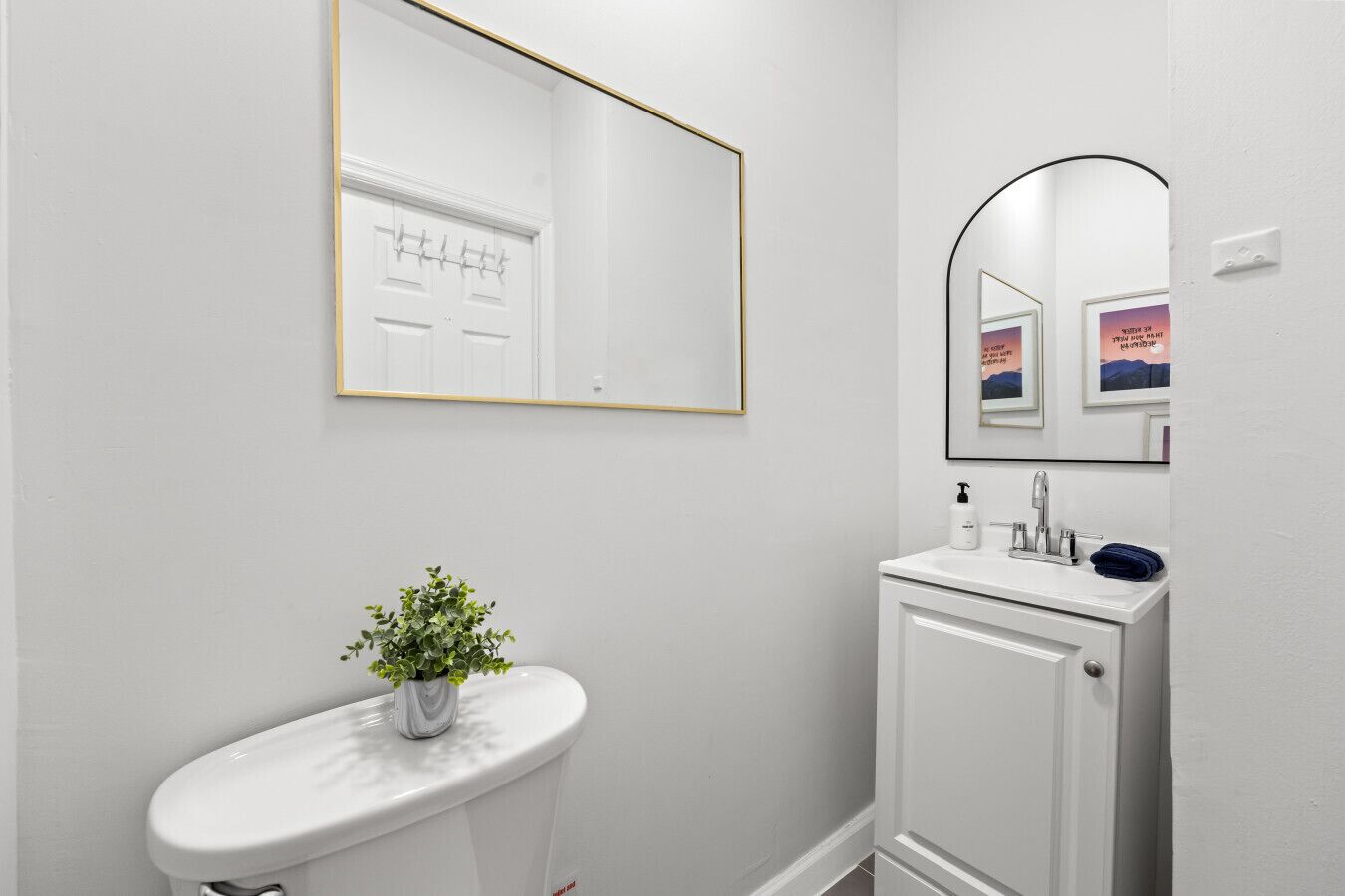 Un baño con inodoro blanco, un lavamanos pequeño con espejo y una planta en maceta.