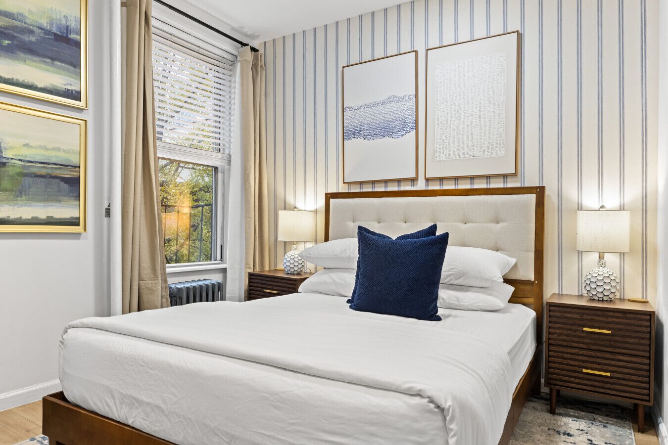 Una habitación de hotel con una cama grande, dos mesitas de noche, un ventanal con cortinas y dos cuadros enmarcados en la pared.