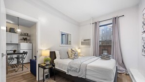 Quarto moderno com cama, mesa de cabeceira, abajur e vista da cidade pela janela.
