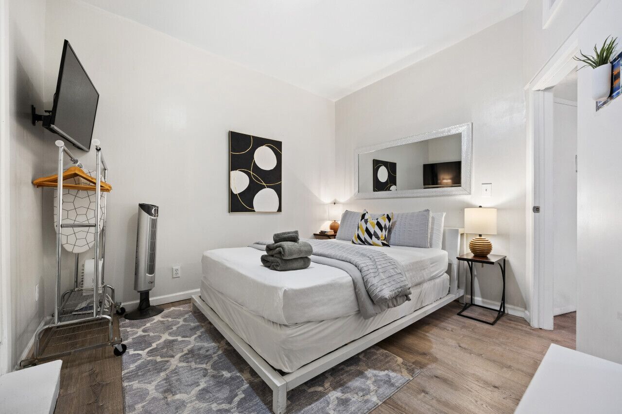 Une chambre à coucher moderne avec un lit, une table de chevet, une lampe et une œuvre d’art.