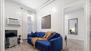 Uma sala de estar moderna com um sofá azul, uma televisão de tela plana, um objeto decorativo na parede e um espelho.