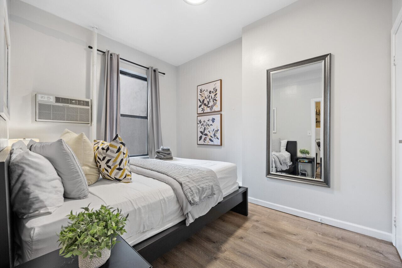 Un dormitorio moderno con cama, sofá, un espejo grande y obras de arte en la pared.