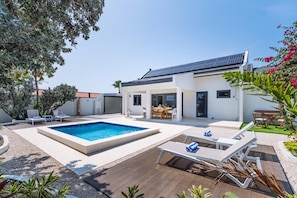 Una casa moderna con piscina, mobiliario de exterior y jardín.