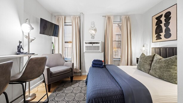 A hotel room with a bed, a desk, a chair, a TV, and a window with curtains. - Walk to Time Square! Cozy Studio (New York)