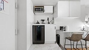 A compact kitchen with a built-in microwave, a dishwasher, and a coffee maker. There are two bar stools and a small table. - Walk to Time Square! Cozy Studio (New York)