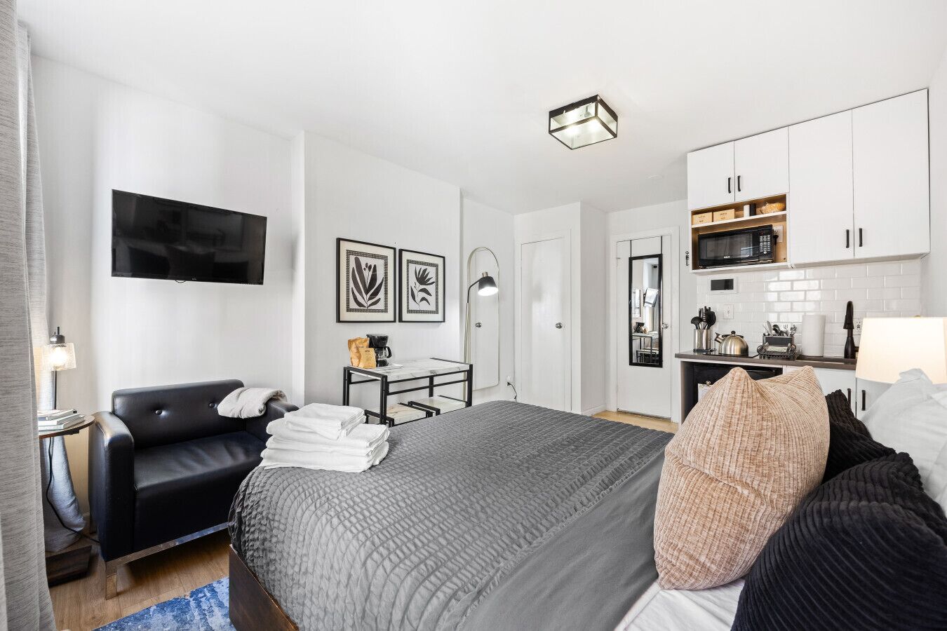 A modern hotel room with a bed, a desk, a flat-screen TV, a kitchenette, and a bathroom.