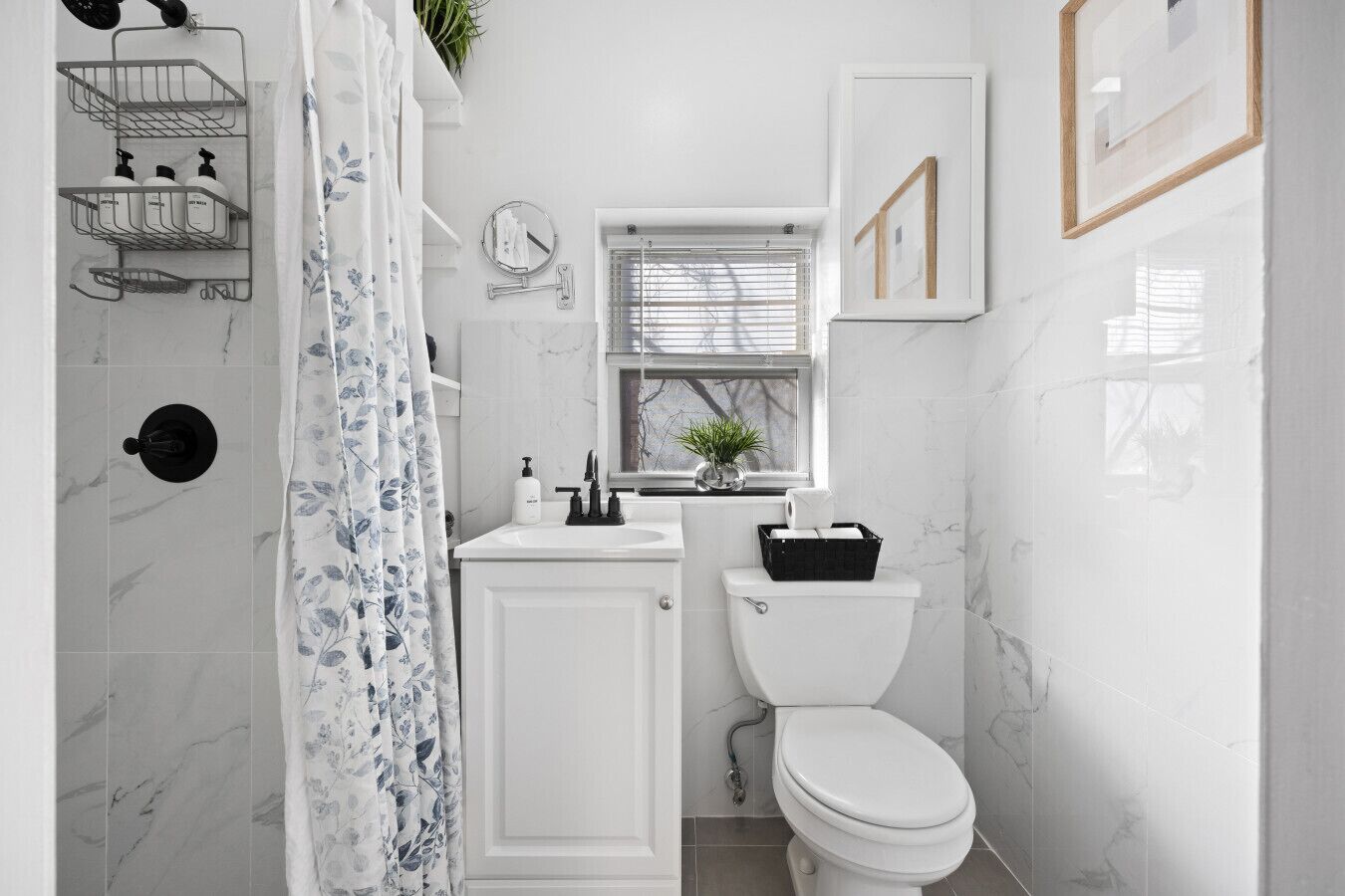 A bathroom with a shower, toilet, sink, and a window with blinds.