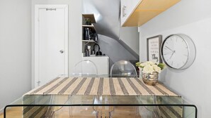 A compact kitchen with a glass table, a clock, and a shelf with kitchen appliances. - Studio Near Restaurants, Broadway, & Shopping (New York)