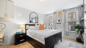 A modern bedroom with a bed, bedside tables, a mirror, and a window with curtains. - Studio Near Restaurants, Broadway, & Shopping (New York)