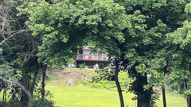 A house with a red roof and a balcony, surrounded by trees and a grassy area.