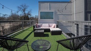 Un patio exterior con un conjunto de sofá, dos sillones de ratán negro, una mesa redonda y un ventanal grande.