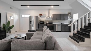 Una sala de estar moderna con un sofá gris, una mesa de centro y una cocina al fondo.