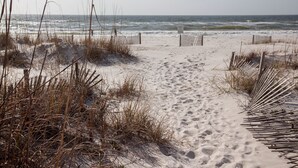A sandy beach path leading to the ocean, surrounded by dry grass and wooden barriers. - Sea Monster, West. Big. Beachfront. Pool. Sleeps 26. Awesome location! (Gulf Shores)